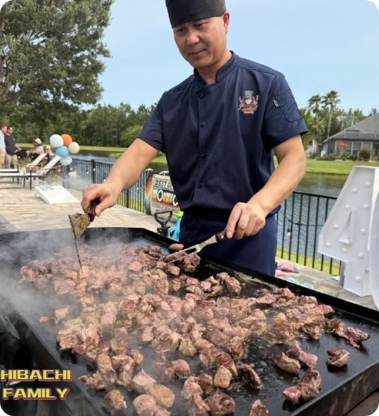 Hibachi chef grilling steak cubes on a large outdoor griddle