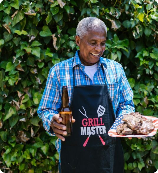 Hibachi grill master smiling while holding a beer and plate of steak outdoors